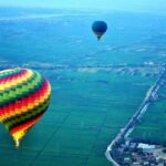 La piana coltivata del Nilo a Luxor vista dall'alto all'alba, con i campi verdi fino al fiume e due mongolfiere in volo