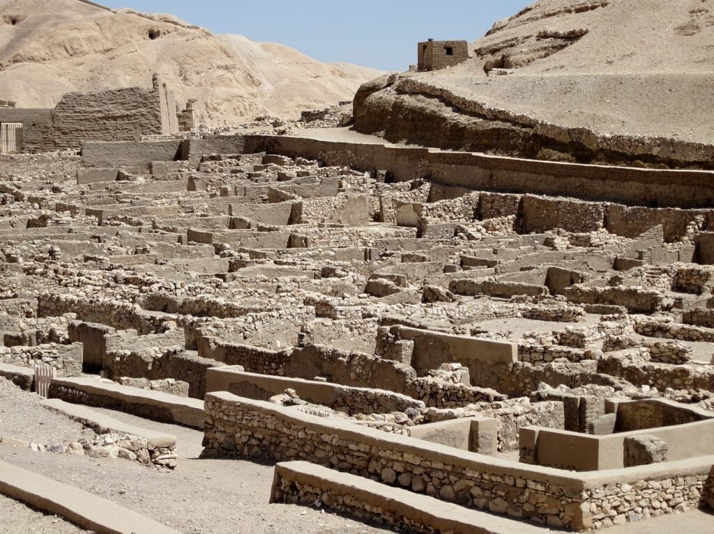 Il villaggio operaio di Deir el-Medina scavato, con le case allineate lungo la strada centrale e le colline tebane sullo sfondo