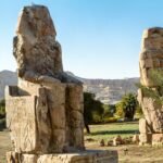 I due Colossi di Memnone nella luce calda del mattino, con le rupi tebane e le palme sullo sfondo