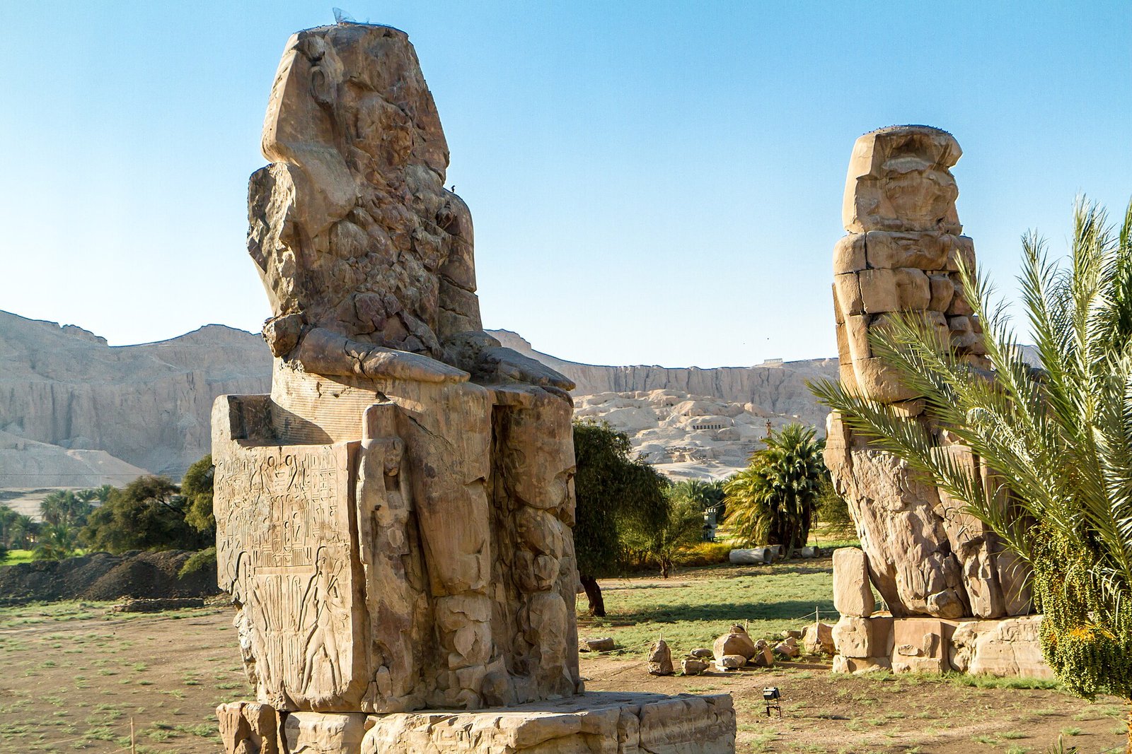 I due Colossi di Memnone nella luce calda del mattino, con le rupi tebane e le palme sullo sfondo