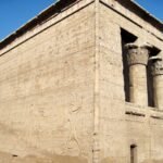 La parete esterna scolpita del tempio di Esna nella luce bassa del pomeriggio, con i capitelli floreali della sala ipostila sullo sfondo