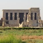 La facciata del tempio di Hathor a Dendera con i capitelli hathorici, vista dai campi coltivati che circondano il sito