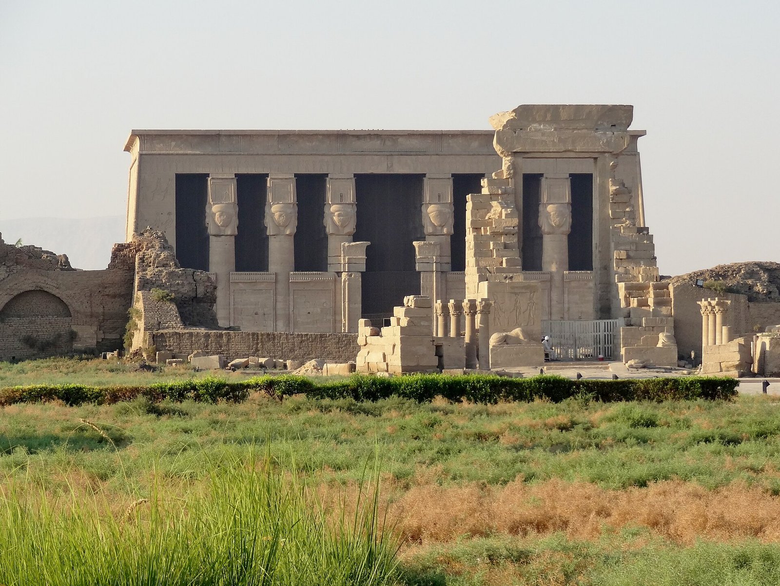 La facciata del tempio di Hathor a Dendera con i capitelli hathorici, vista dai campi coltivati che circondano il sito
