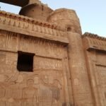 La parete scolpita del tempio di Kom Ombo con la cornice a gola egizia e le colonne sullo sfondo, nella luce calda del tardo pomeriggio