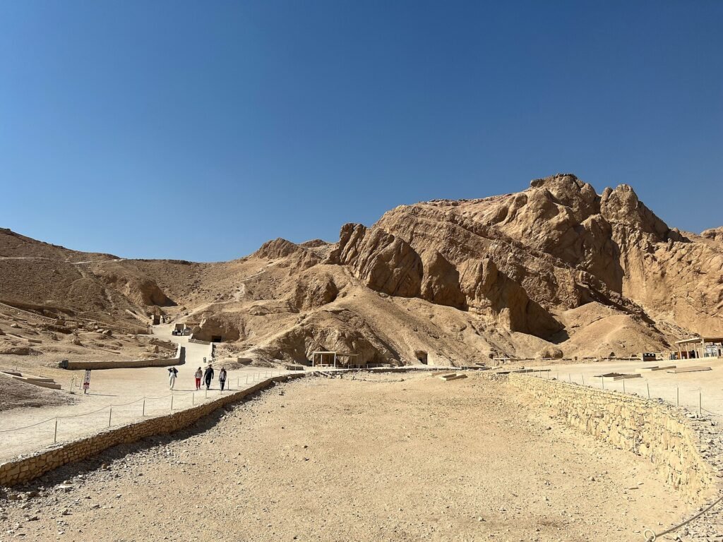 La Valle delle Regine a Luxor ovest, con la parete rocciosa erosa, i sentieri sul fondo del vallone e alcuni visitatori in lontananza