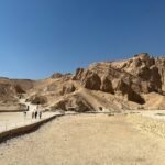 La Valle delle Regine a Luxor ovest, con la parete rocciosa erosa, i sentieri sul fondo del vallone e alcuni visitatori in lontananza