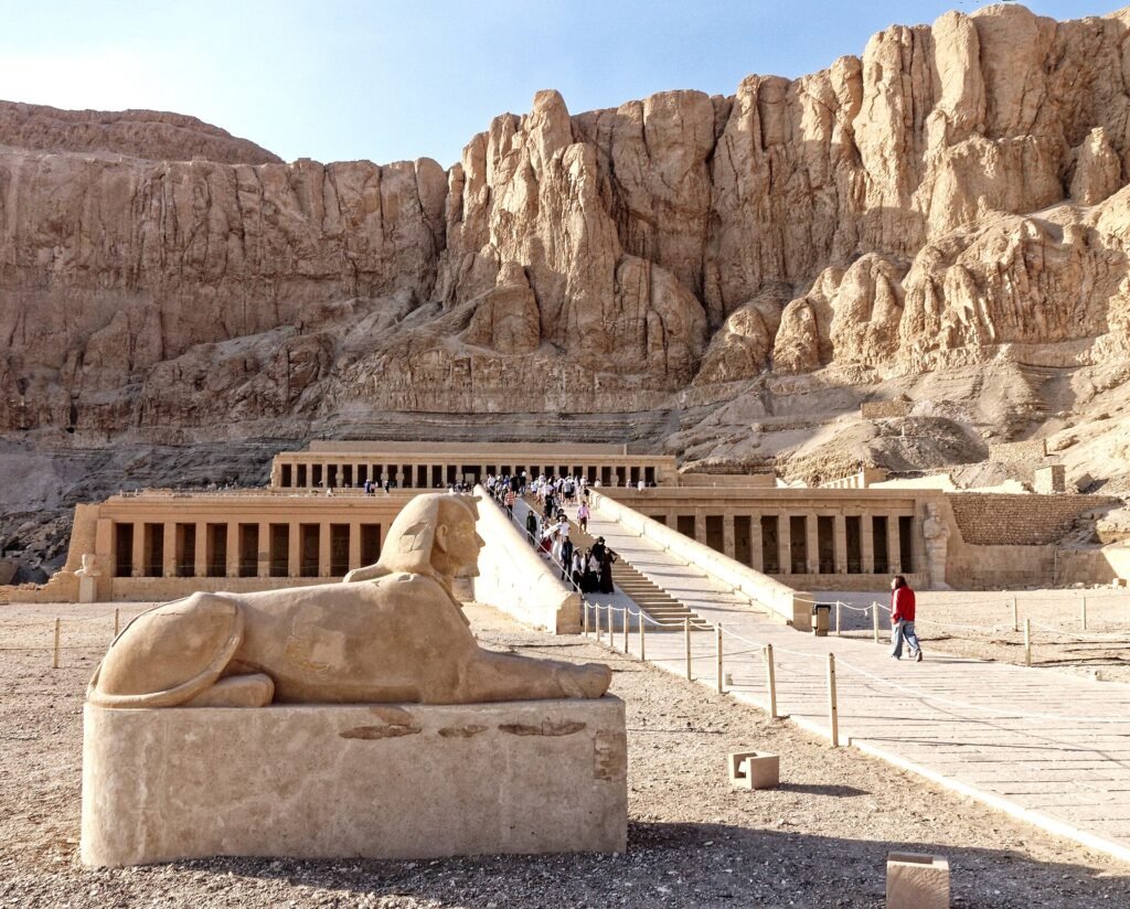 Il tempio di Hatshepsut a Deir el-Bahari visto di fronte, con le terrazze e i colonnati ai piedi della parete rocciosa e una sfinge in primo piano