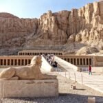 Il tempio di Hatshepsut a Deir el-Bahari visto di fronte, con le terrazze e i colonnati ai piedi della parete rocciosa e una sfinge in primo piano