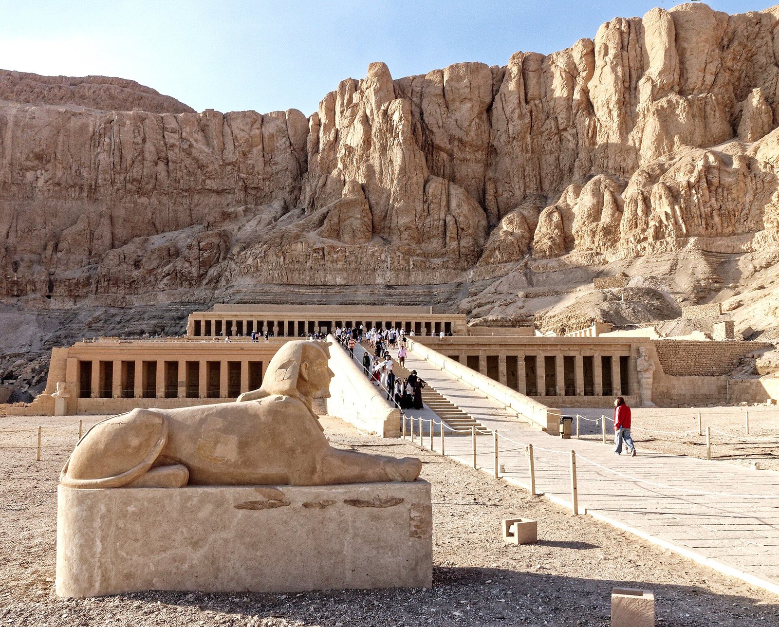 Il tempio di Hatshepsut a Deir el-Bahari visto di fronte, con le terrazze e i colonnati ai piedi della parete rocciosa e una sfinge in primo piano