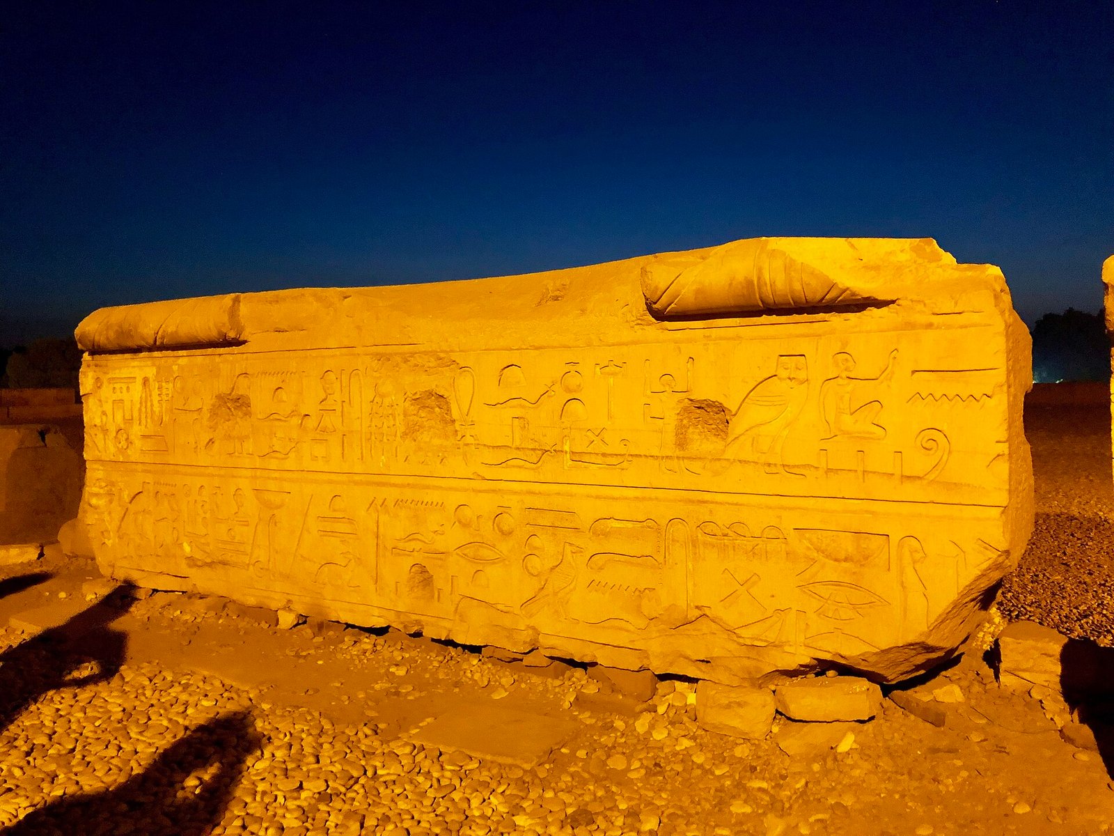 Un grande architrave scolpito caduto a terra fra le rovine di Kom Ombo, illuminato di notte contro il cielo blu
