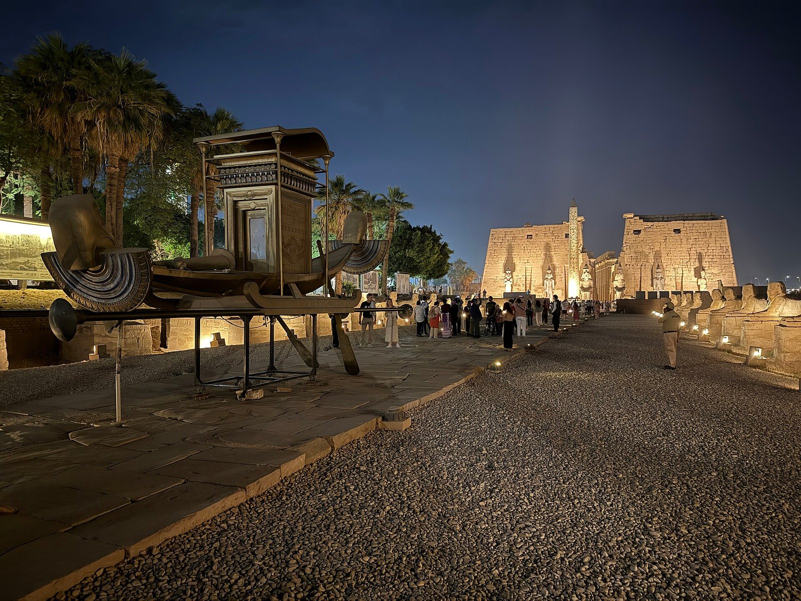 Il tempio di Luxor illuminato di sera, con la riproduzione della barca sacra in primo piano, il viale delle sfingi sulla destra e il pilone con l'obelisco sullo sfondo