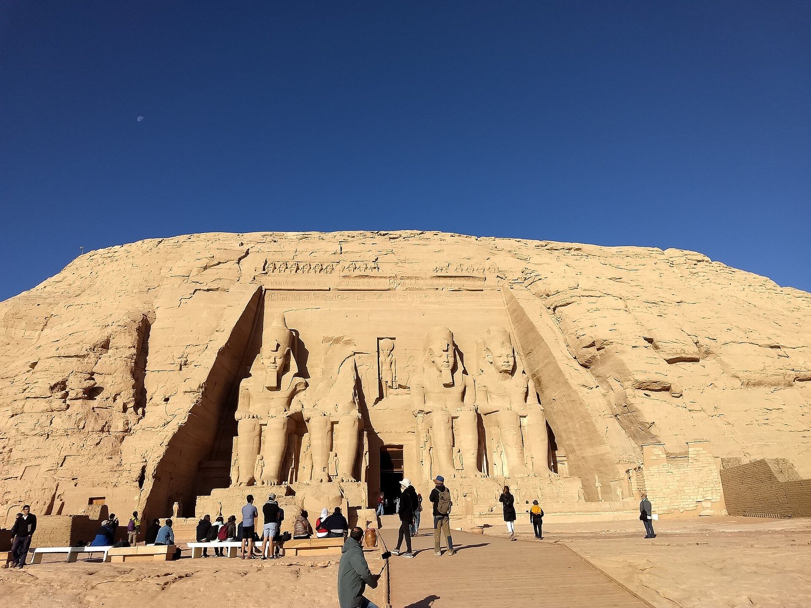 La facciata del Grande Tempio di Abu Simbel scavata nella roccia, con i colossi seduti e i visitatori davanti all'ingresso