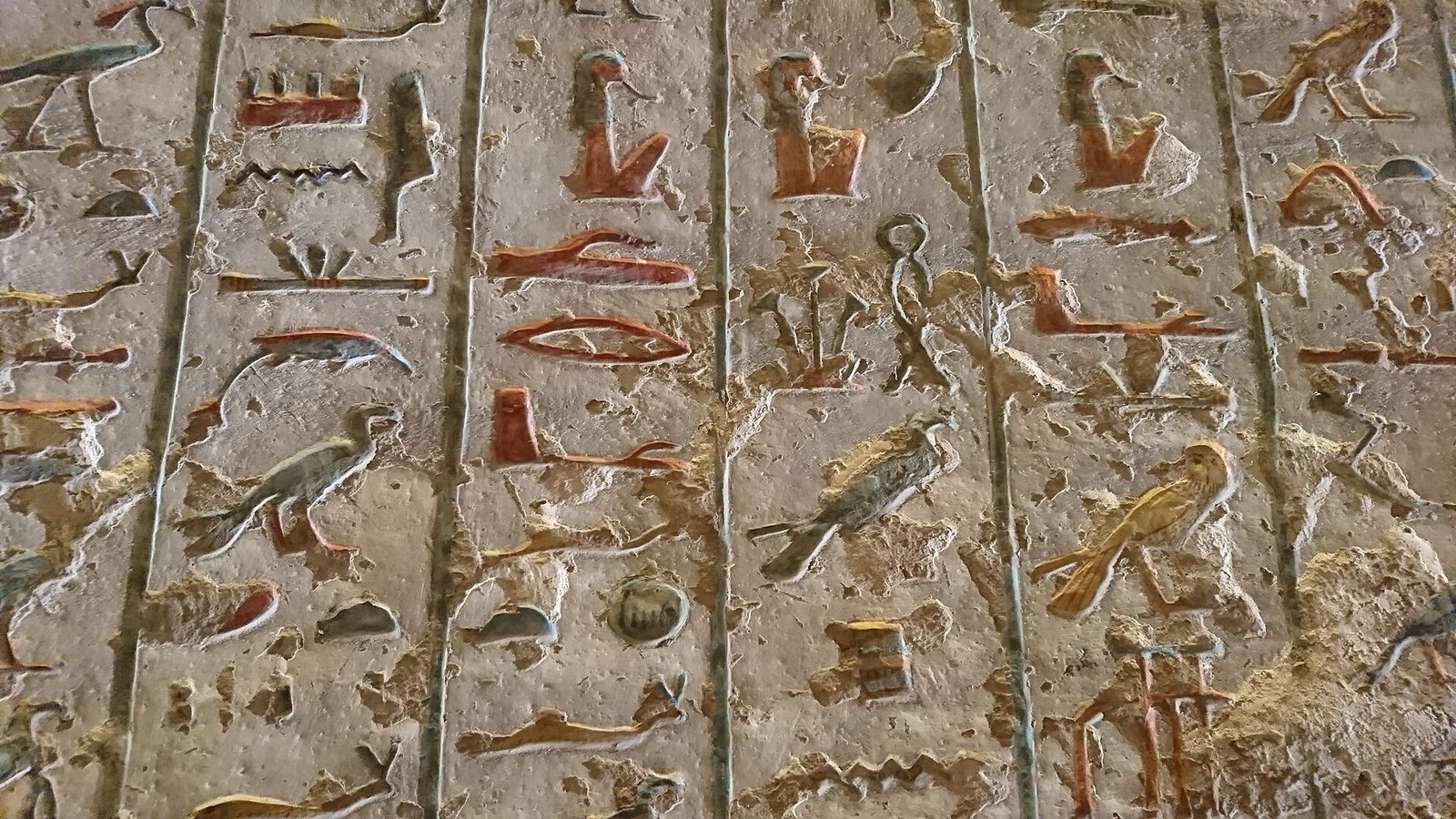 Geroglifici scolpiti a rilievo con tracce del colore originale su una parete di tomba nella Valle dei Re, con la superficie in parte consumata