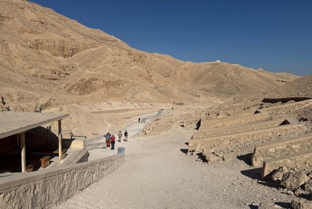 La Valle delle Regine vista d'insieme, con il sentiero che risale fra le colline desertiche e le tettoie sugli ingressi delle tombe