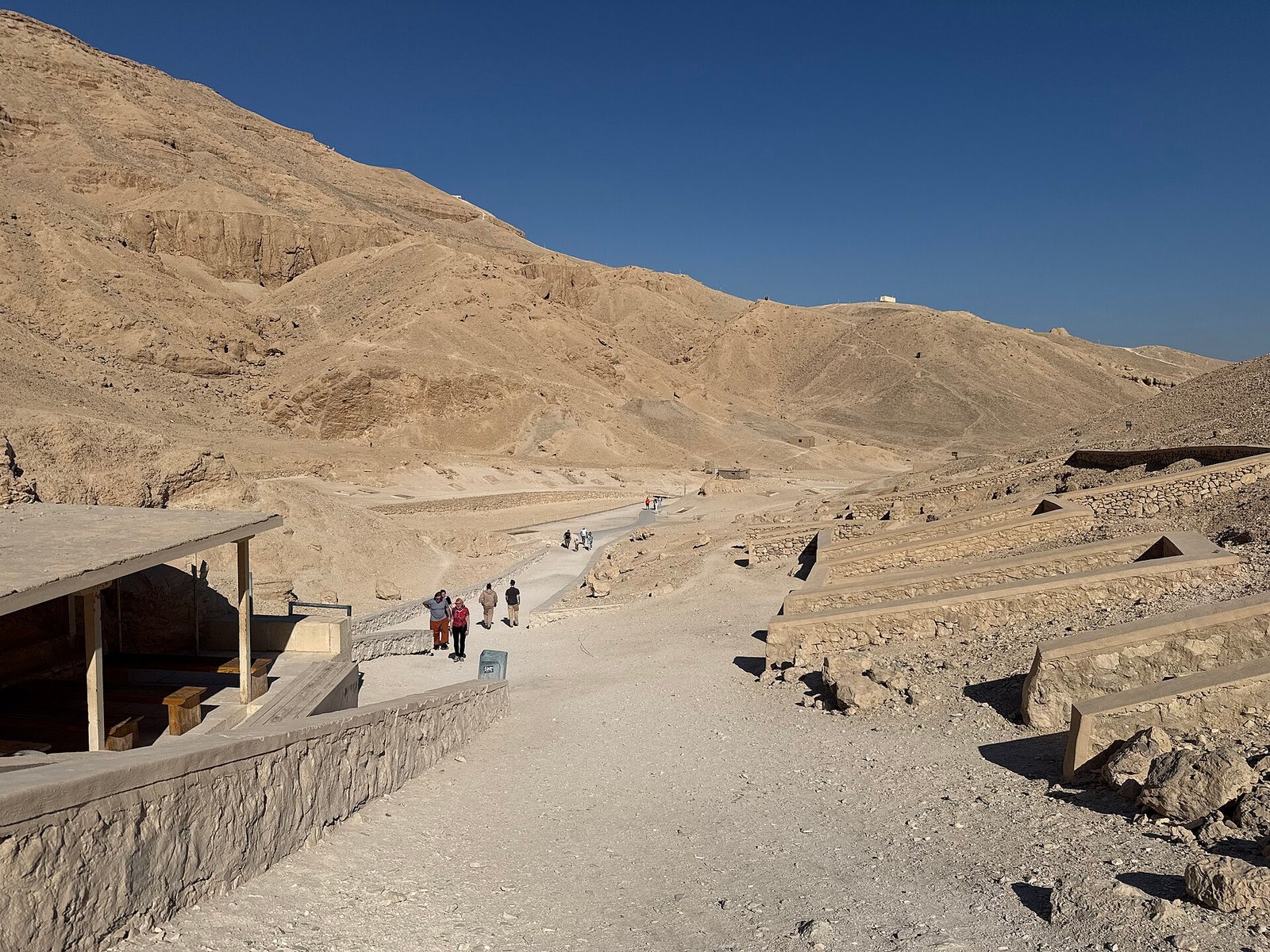 La Valle delle Regine vista d'insieme, con il sentiero che risale fra le colline desertiche e le tettoie sugli ingressi delle tombe