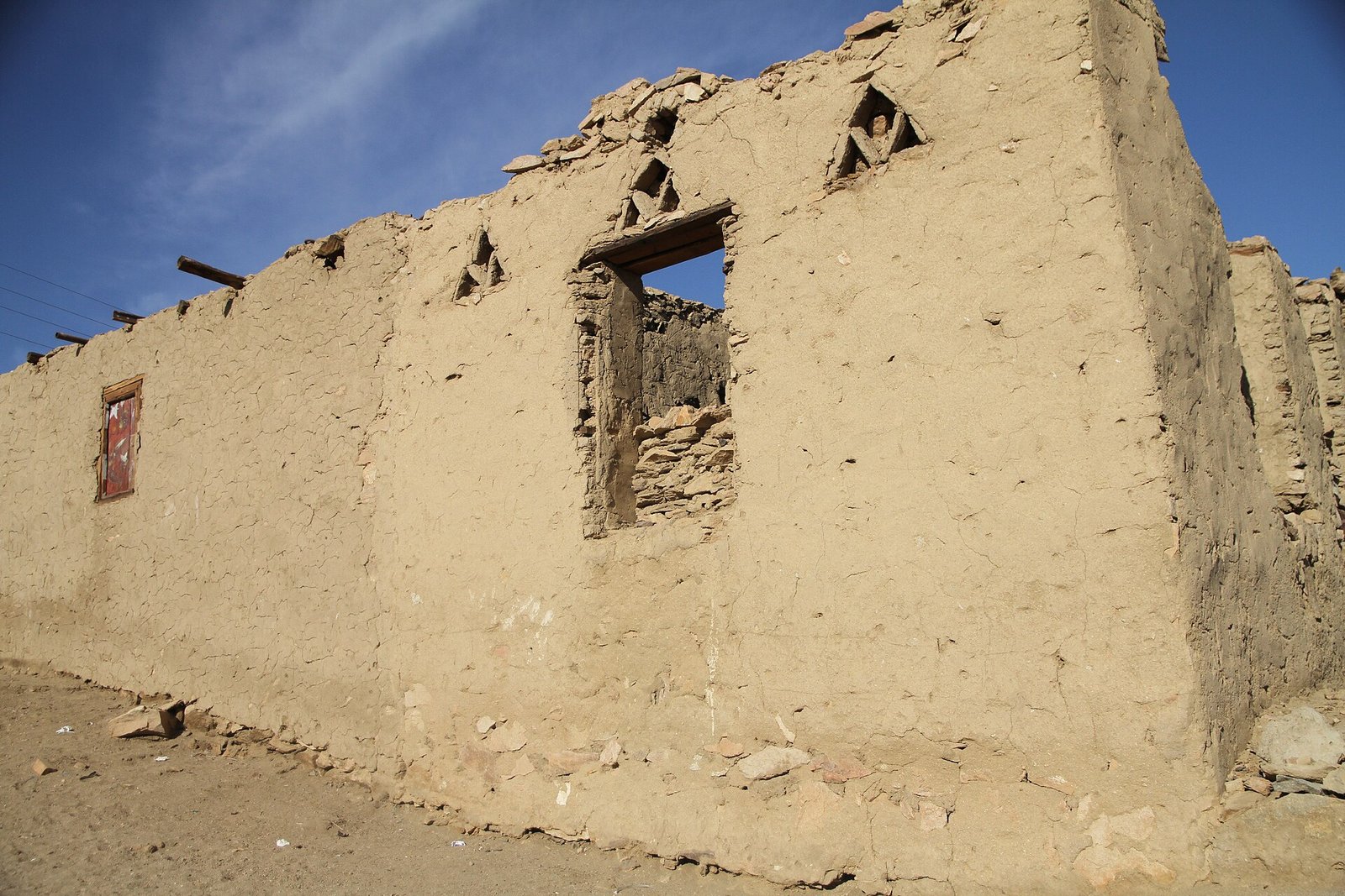 Il muro in mattoni di fango di una casa nubiana, con gli architravi in legno sopra le aperture e il pietrame a vista alla base