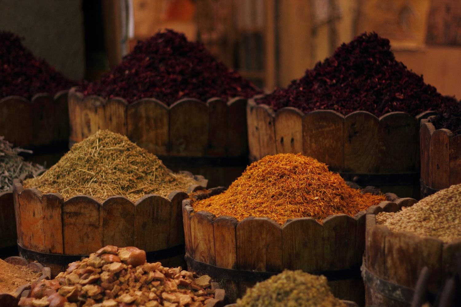Tini di legno colmi di spezie in un mercato egiziano, con ibisco essiccato, fiori di cartamo e erbe aromatiche nella luce calda