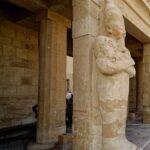 Una statua osiriaca addossata a un pilastro nel tempio di Hatshepsut, con le braccia incrociate sul petto e tracce di colore rosso sul volto