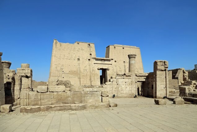 I due piloni d'ingresso del tempio di Edfu visti di fronte, con i resti del cortile in primo piano e il cielo azzurro