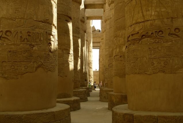 Le colonne coperte di rilievi della grande sala ipostila di Karnak, con alcuni visitatori in fondo alla navata centrale