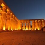 Il colonnato del tempio di Luxor illuminato di notte, con il cielo blu del crepuscolo e alcuni visitatori in lontananza