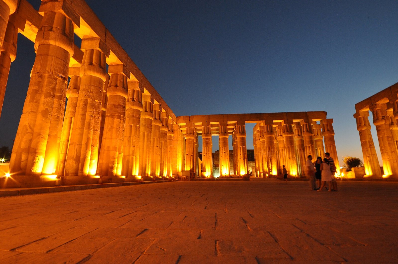 Il colonnato del tempio di Luxor illuminato di notte, con il cielo blu del crepuscolo e alcuni visitatori in lontananza