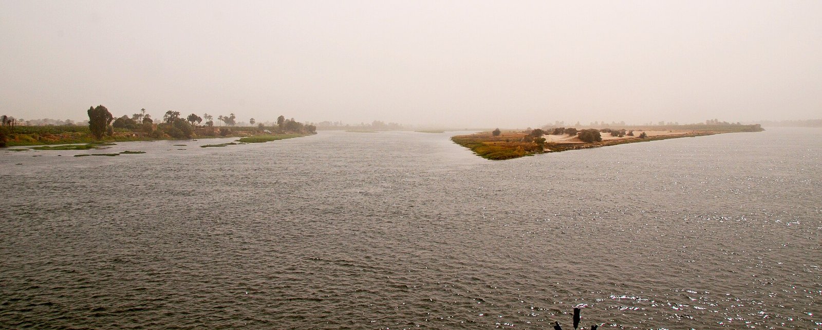 Il Nilo in una giornata velata di foschia, con un isolotto di vegetazione al centro del fiume