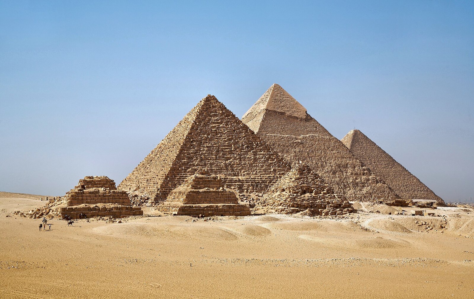 Le tre piramidi di Giza e le piramidi minori viste da sud-ovest, sulla sabbia dorata sotto un cielo azzurro