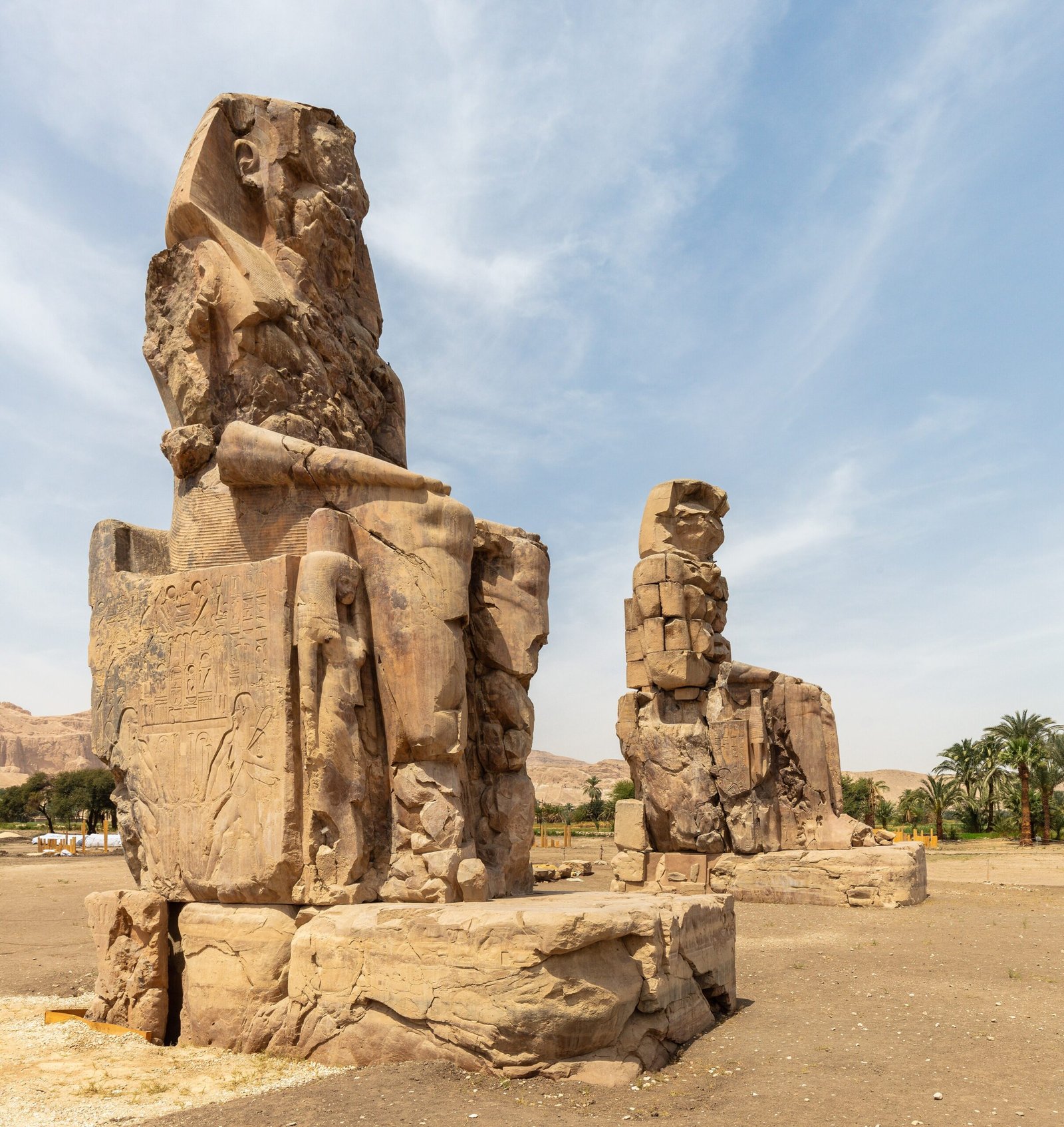 I due Colossi di Memnone in arenaria svettano sulla piana di Luxor sotto un cielo azzurro con nubi sottili