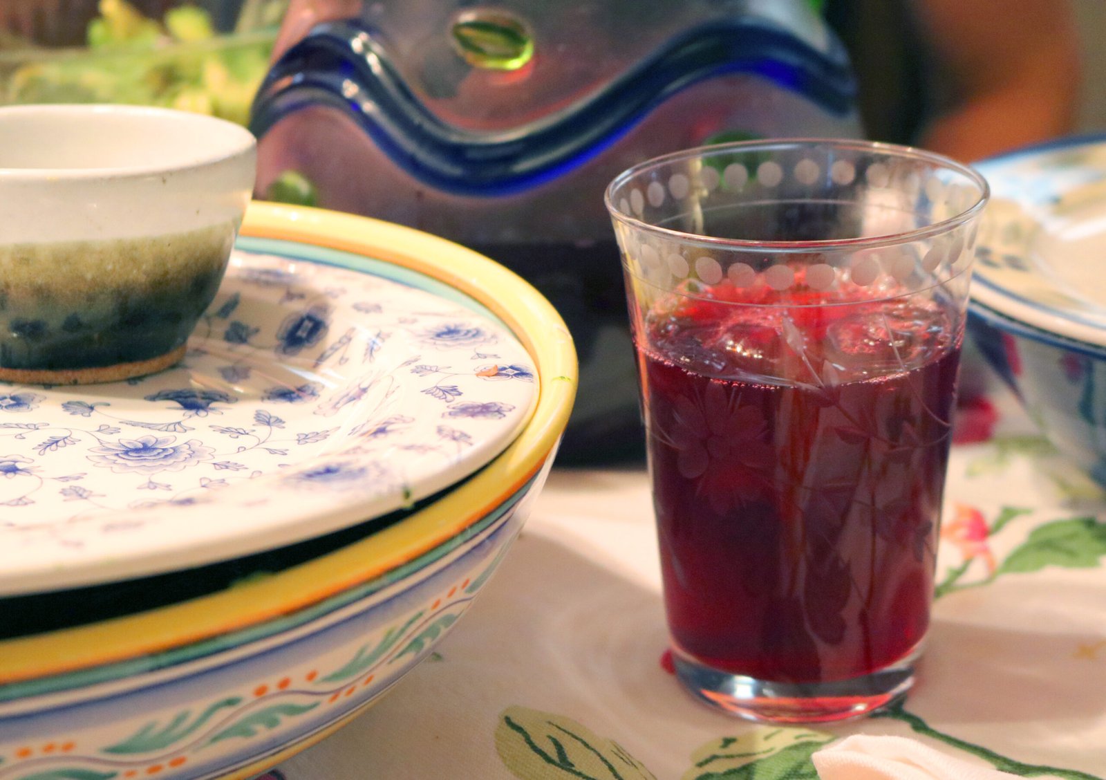 Bicchiere di karkadè rosso accanto a piatti decorati su una tavola apparecchiata