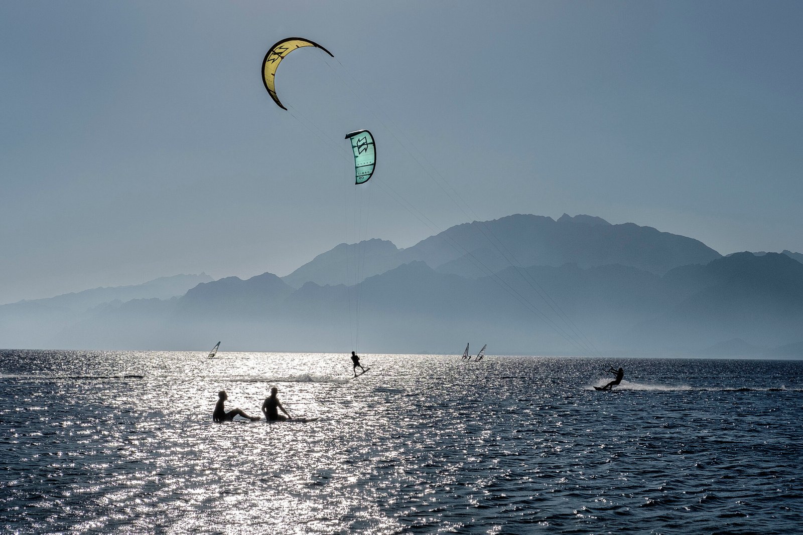 Kitesurfer e windsurfisti in controluce sul mare di Dahab con le montagne della costa opposta del golfo di Aqaba