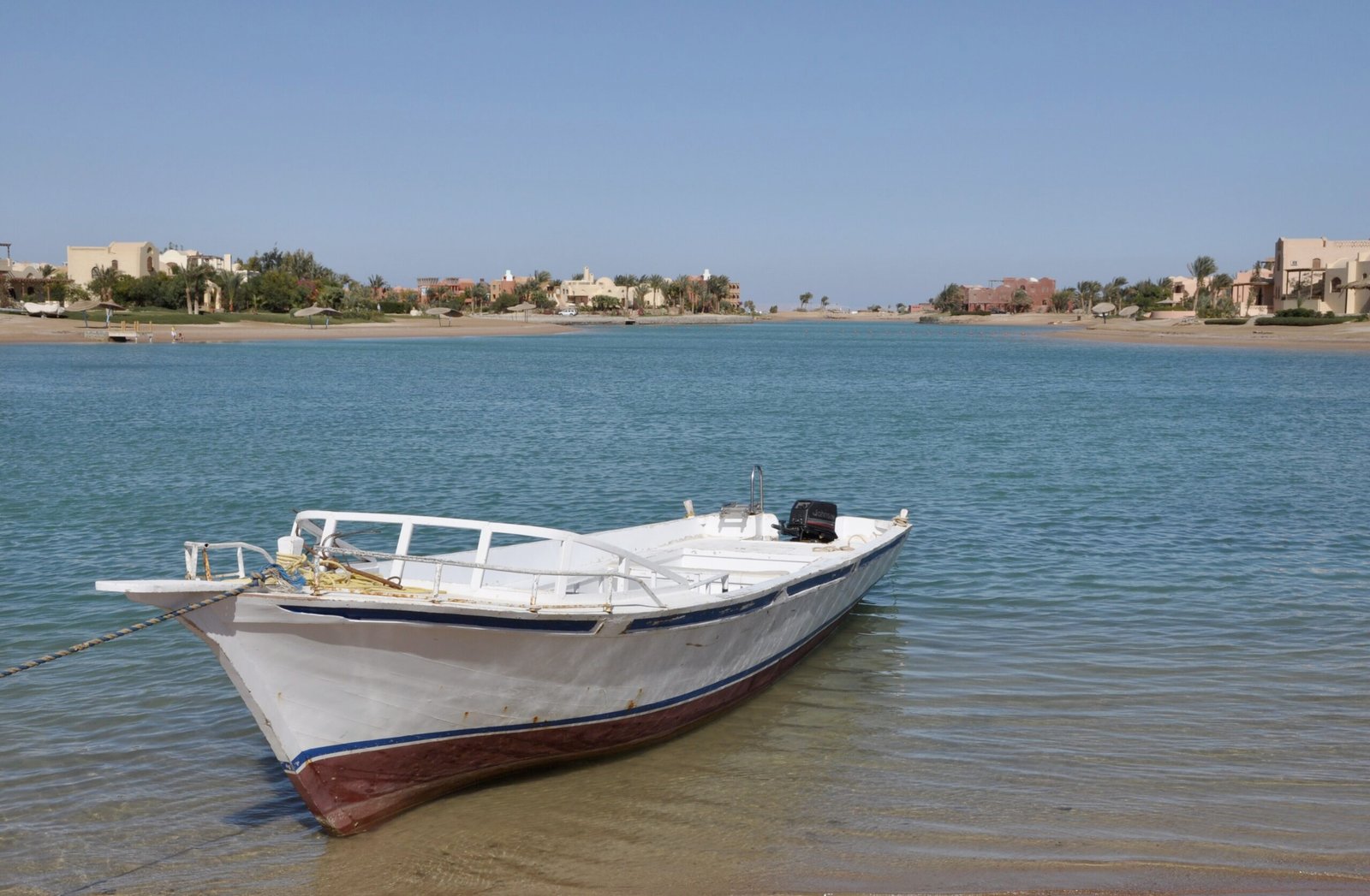 Barca bianca ormeggiata nell'acqua bassa e trasparente della laguna di El Gouna, con il villaggio color sabbia sulla riva opposta