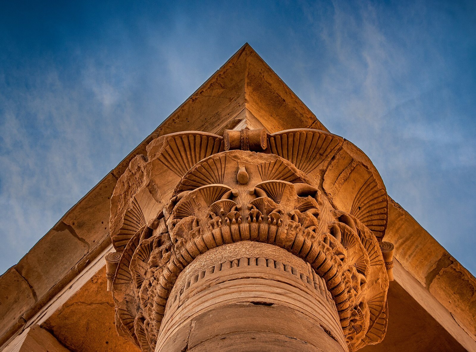 Capitello composito di una colonna di tempio, con foglie di palma e boccioli di loto, ripreso dal basso contro il cielo azzurro