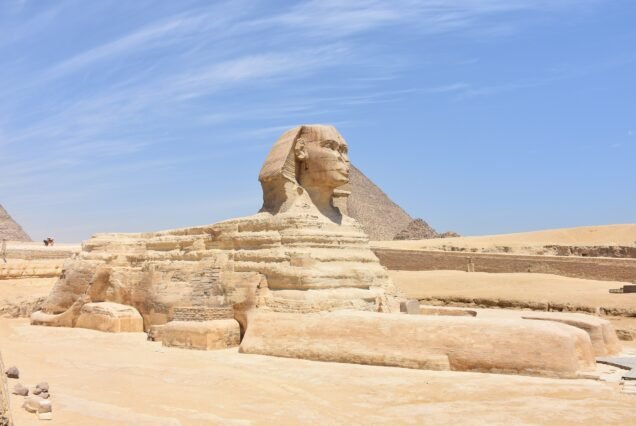 La Sfinge di Giza per intero sulla sabbia deserta, con la piramide di Chefren che si alza dietro.