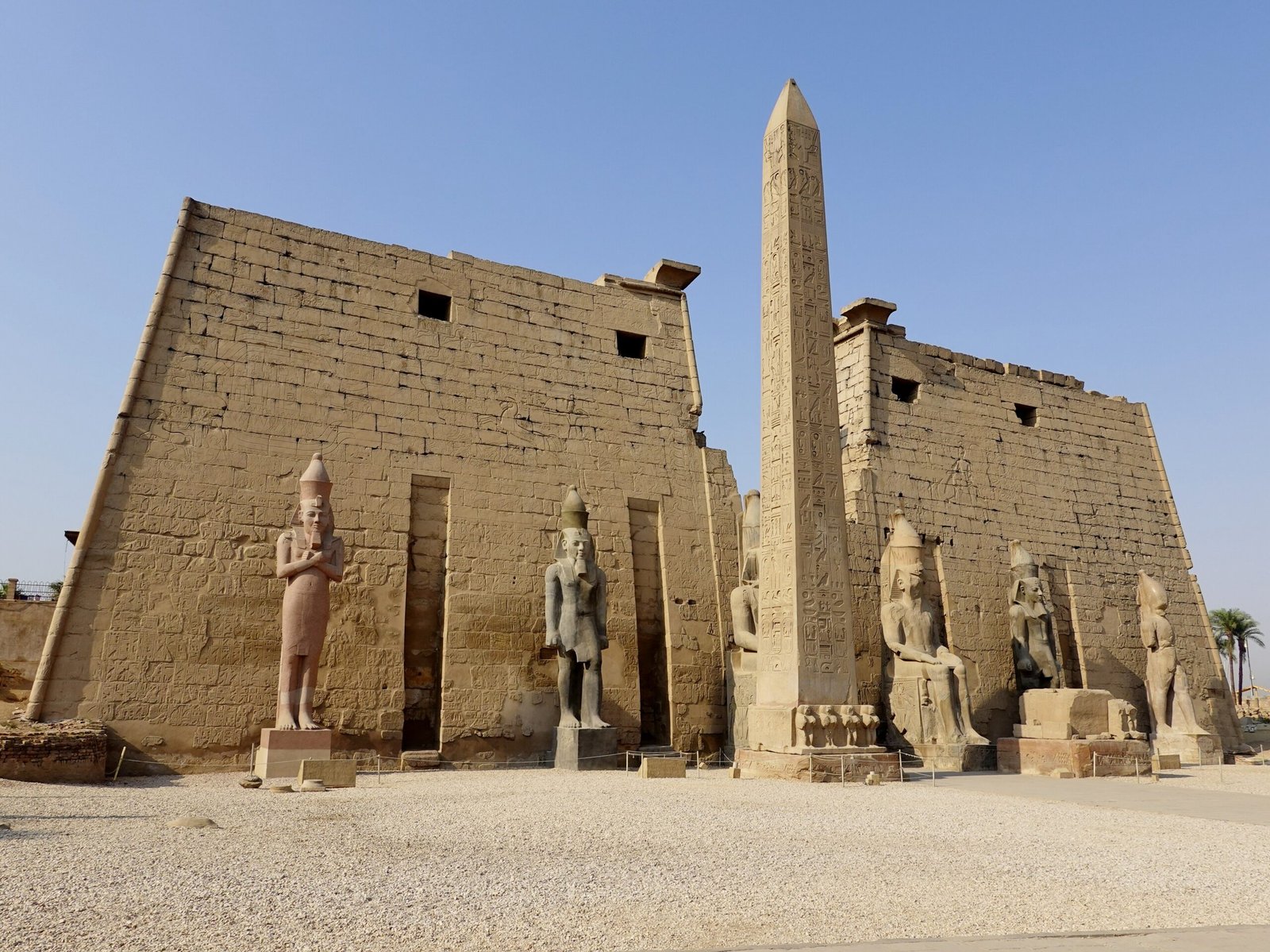 Il primo pilone del Tempio di Luxor con l'obelisco di Ramses II e i colossi seduti sotto un cielo azzurro
