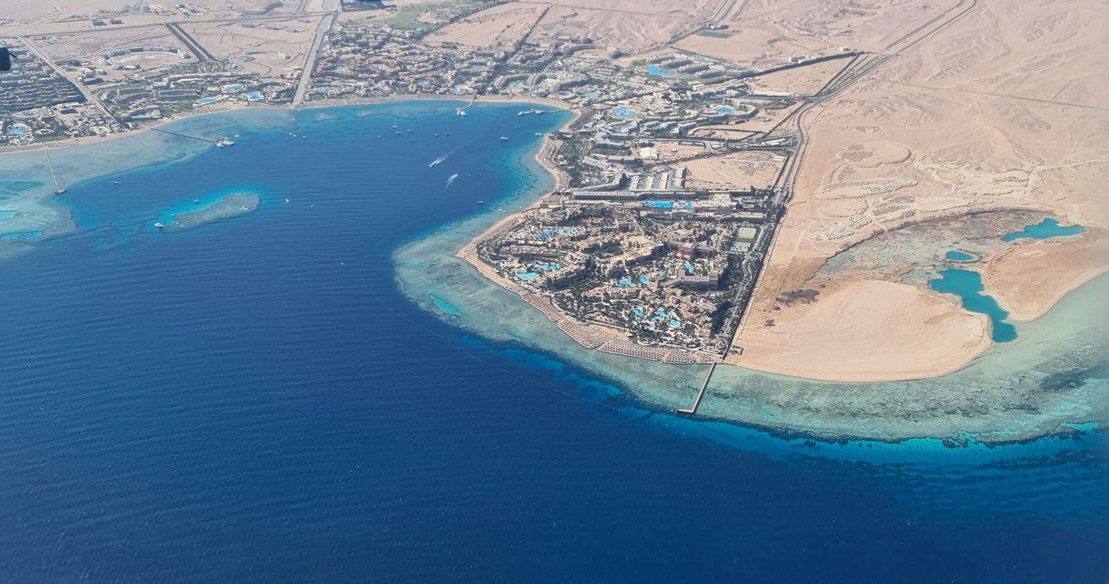 Veduta aerea della baia di Makadi con mare blu profondo, barriera corallina turchese lungo la riva e costa desertica