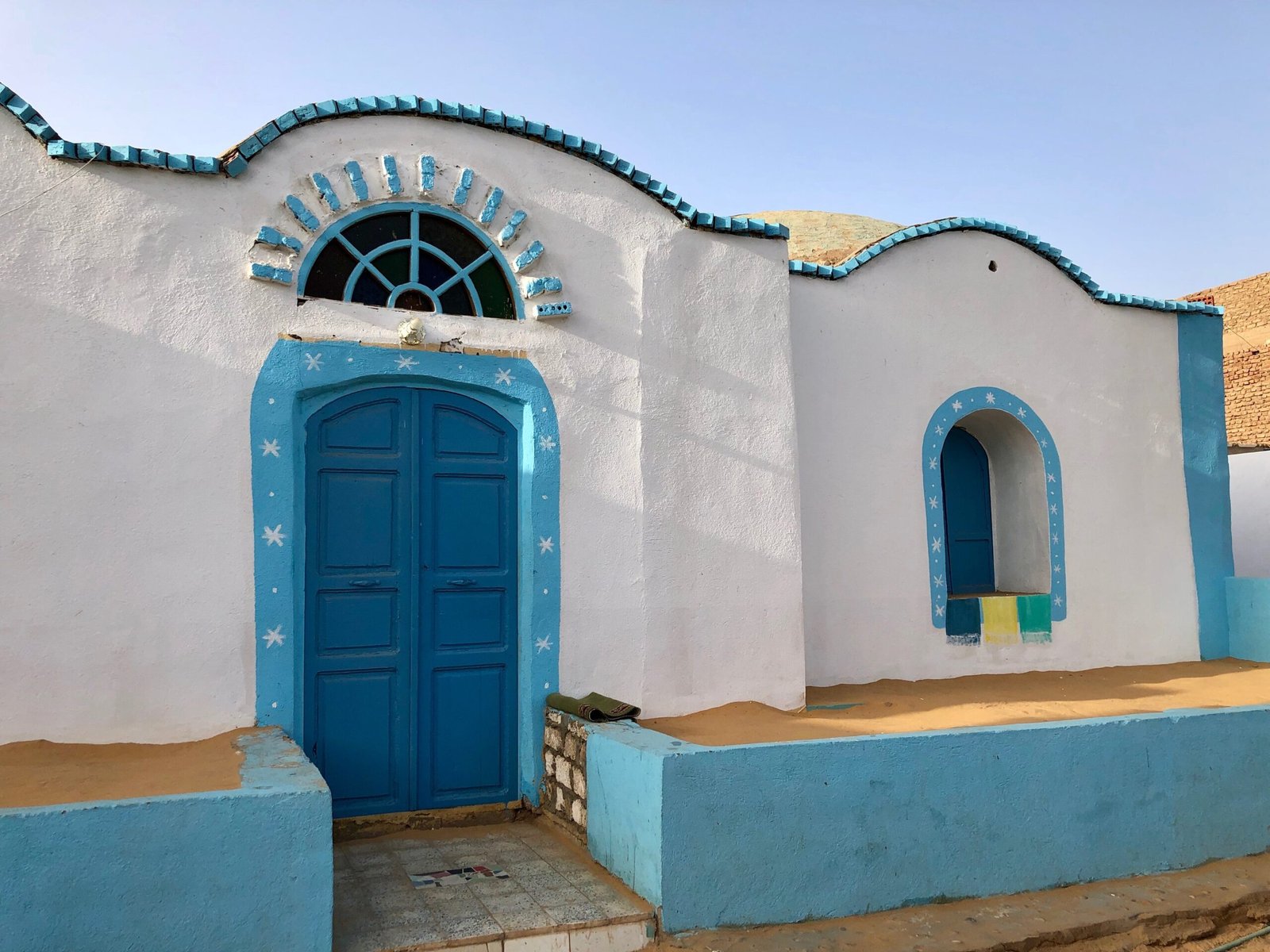 Casa nubiana ad Assuan con facciata bianca e azzurra, portale ad arco e panca in muratura