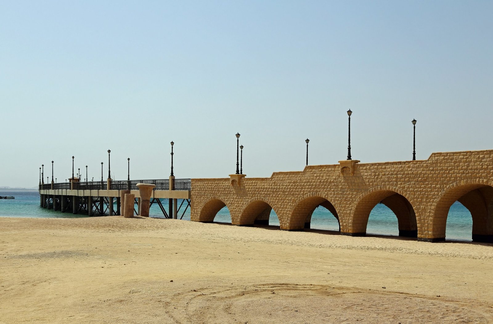 Passerella ad archi in arenaria di Sahl Hasheesh sul mare turchese, con lampioni in ferro e pontile sullo sfondo