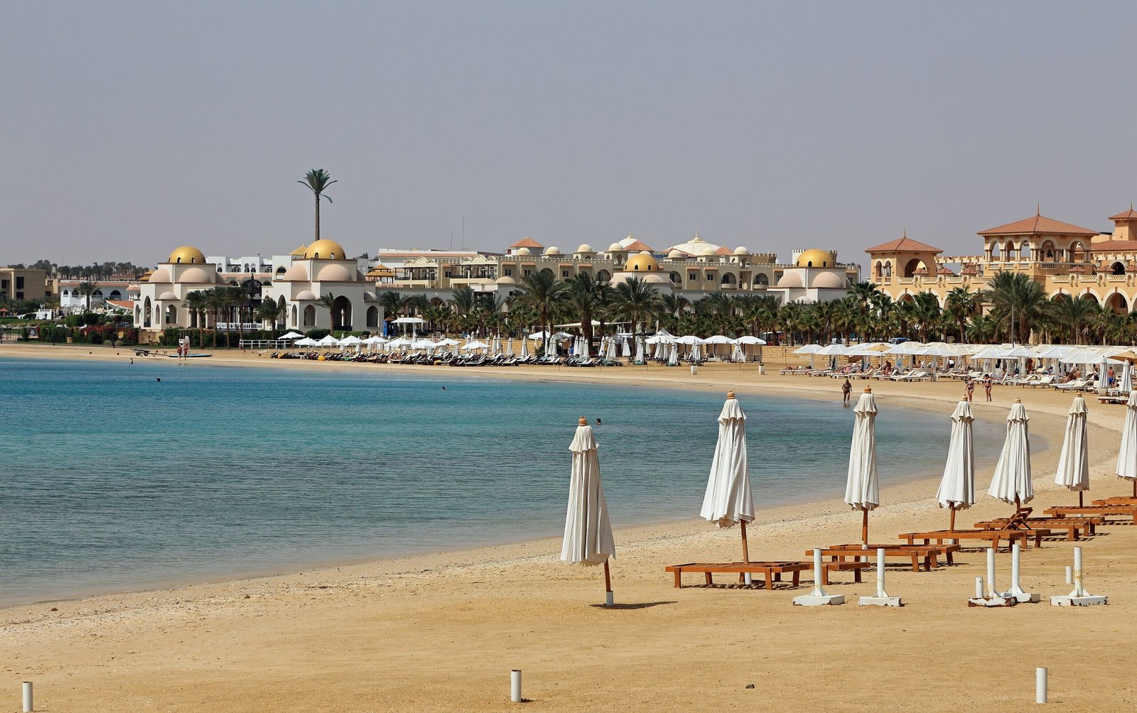 La baia di Sahl Hasheesh con la spiaggia di sabbia, gli ombrelloni chiusi e gli edifici con le cupole dorate sullo sfondo