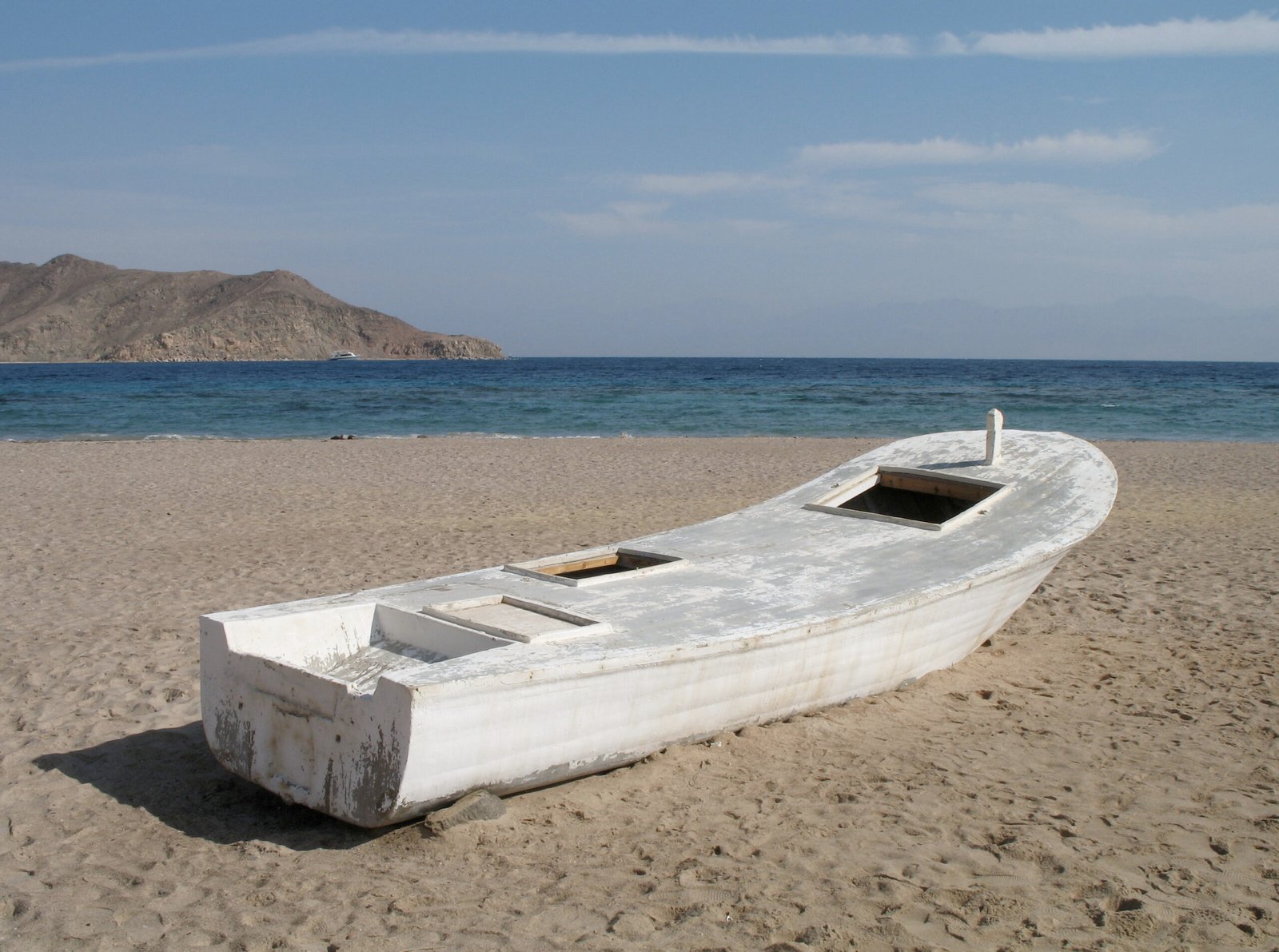 Barca in legno bianca in secca sulla sabbia di una spiaggia di Taba, con il mare del golfo di Aqaba e un promontorio roccioso alle spalle