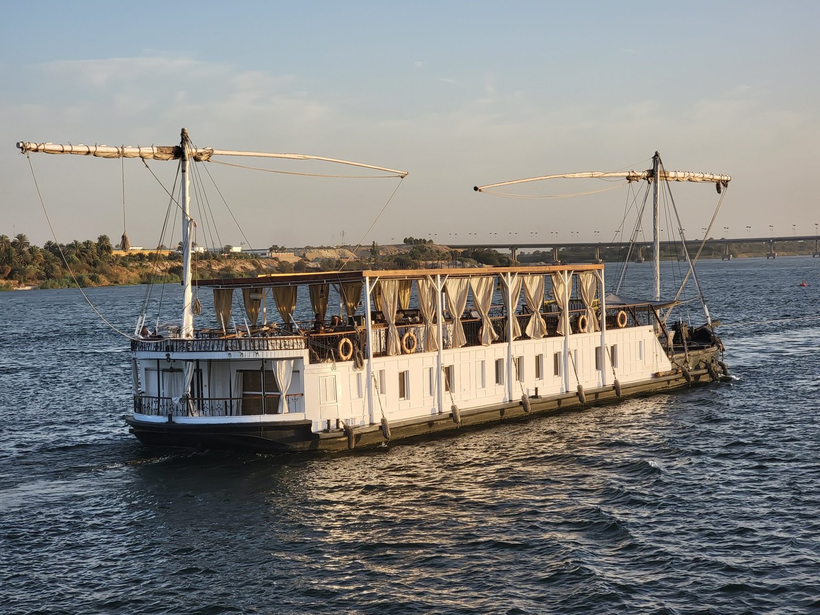 Dahabiya bianca in navigazione sul Nilo con le tende chiare del ponte superiore