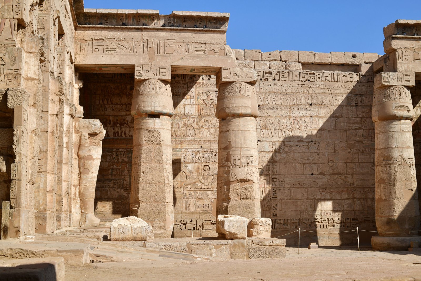 Le grandi pareti scolpite di Medinet Habu viste dal cortile lastricato nella luce calda