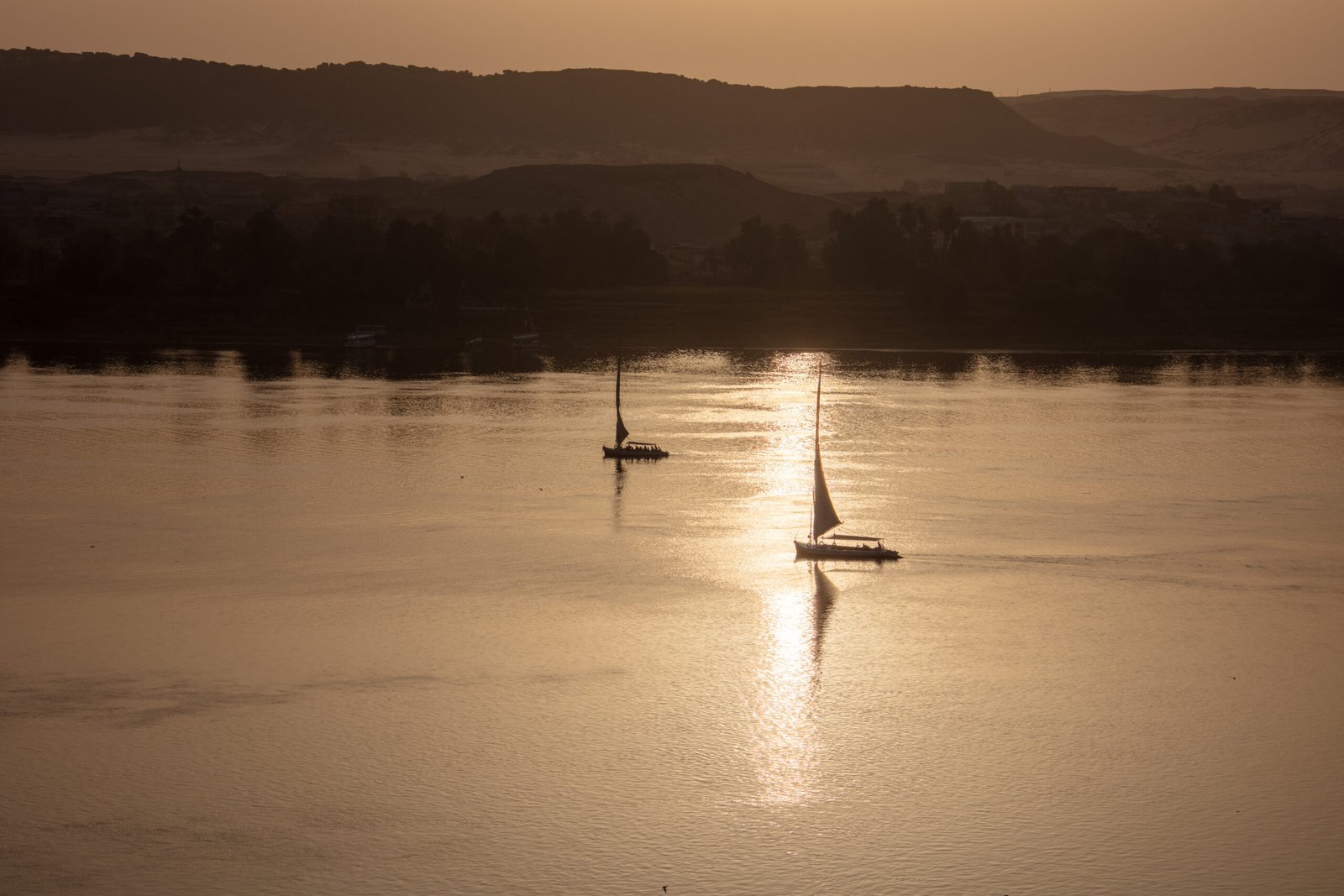 Feluche a vela sul Nilo ad Assuan nella luce bassa del tramonto, con la riva desertica sullo sfondo