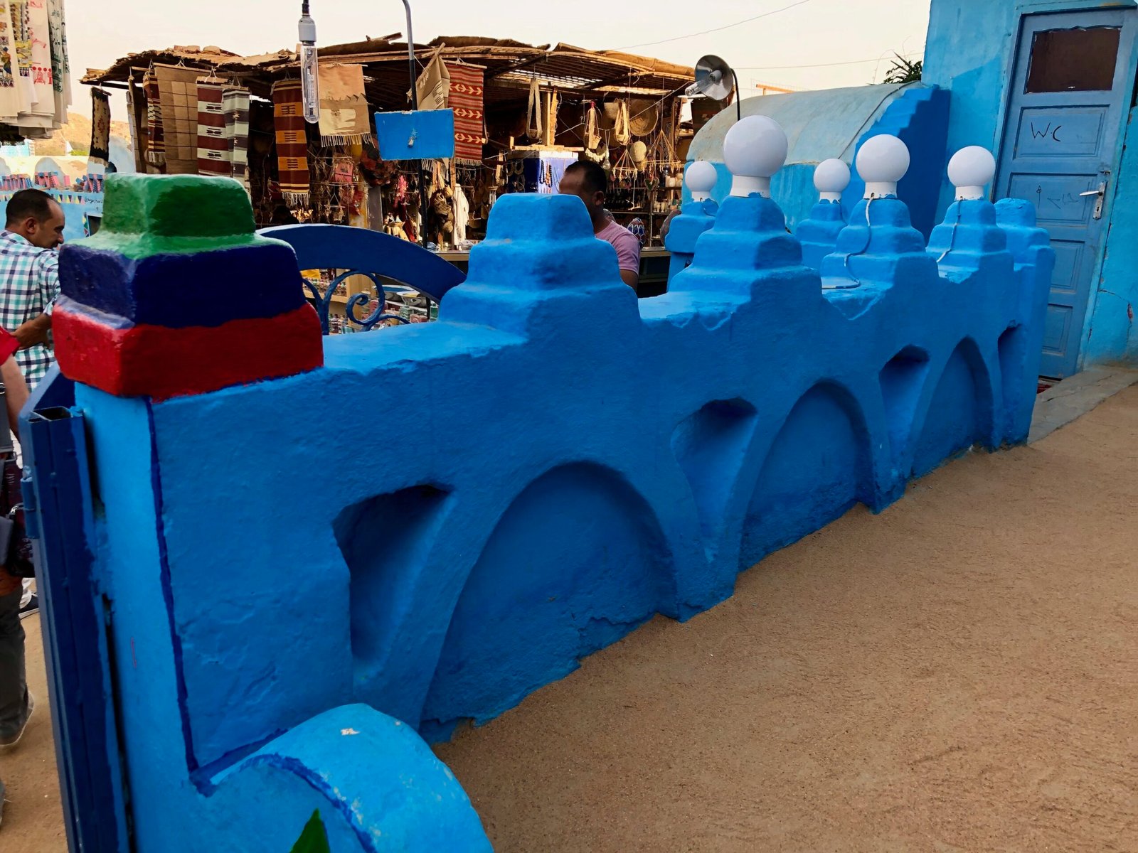 Un muretto azzurro con archi e pinnacoli in un villaggio nubiano, con le bancarelle sullo sfondo