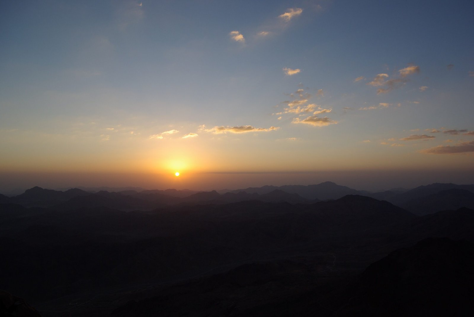 Il sole che sorge tra le nuvole sottili sopra le montagne del Sinai, visto dalla cima del Monte Sinai