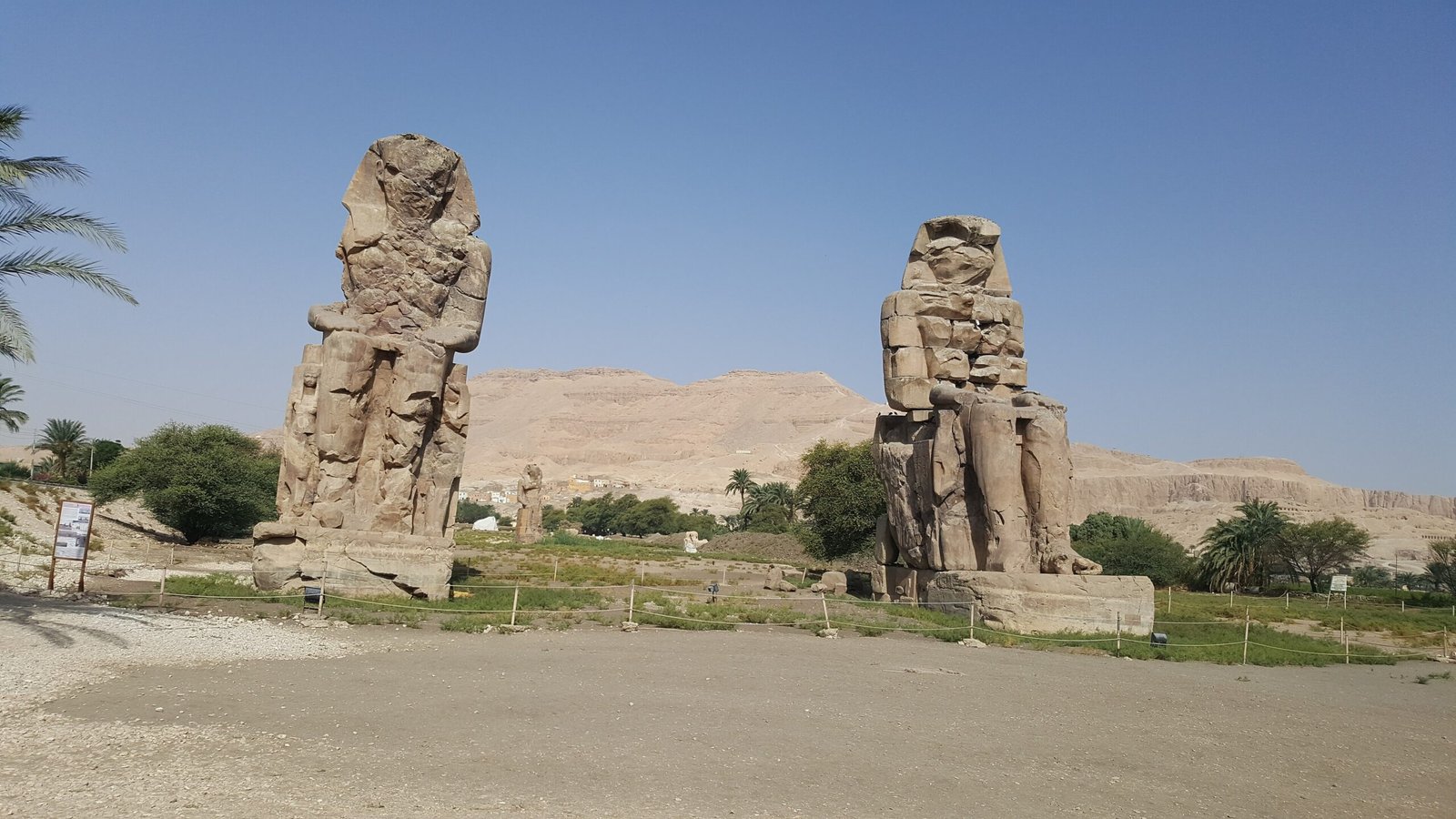 I due Colossi di Memnone davanti alla falesia tebana, con le palme e il cielo azzurro