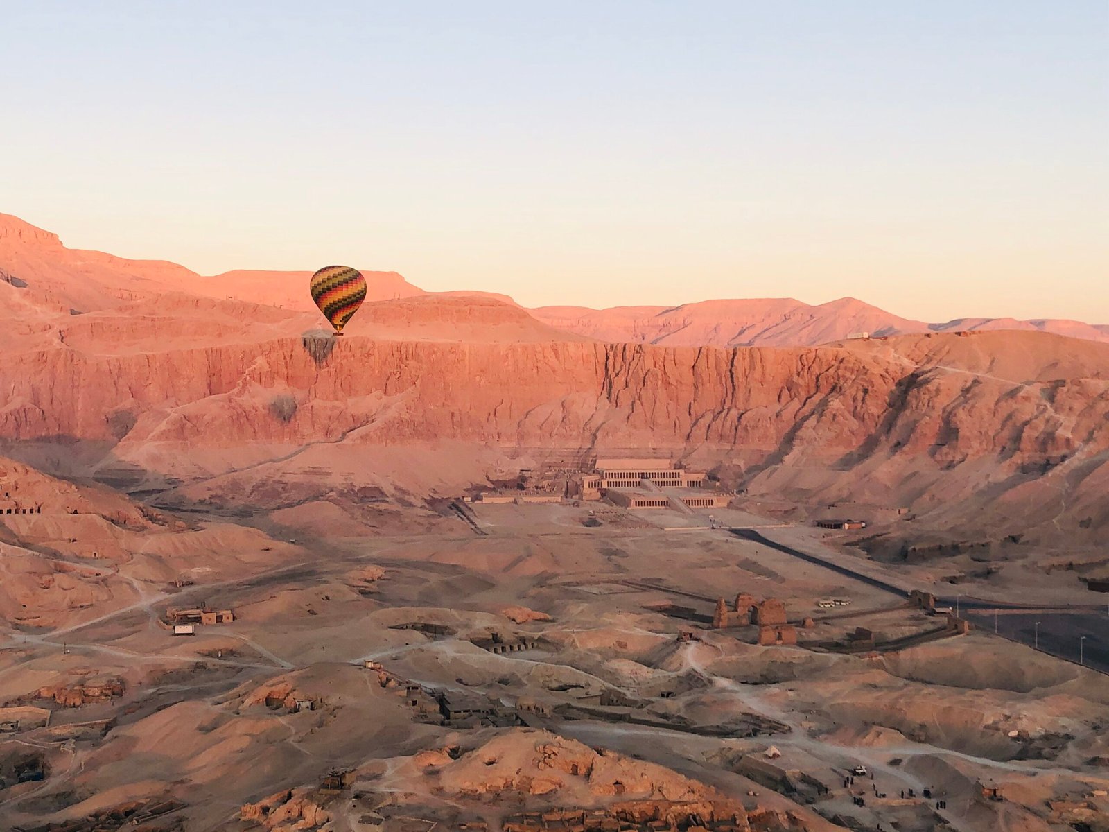 Una mongolfiera sopra la riva ovest di Luxor all'alba, con il tempio di Hatshepsut ai piedi della falesia