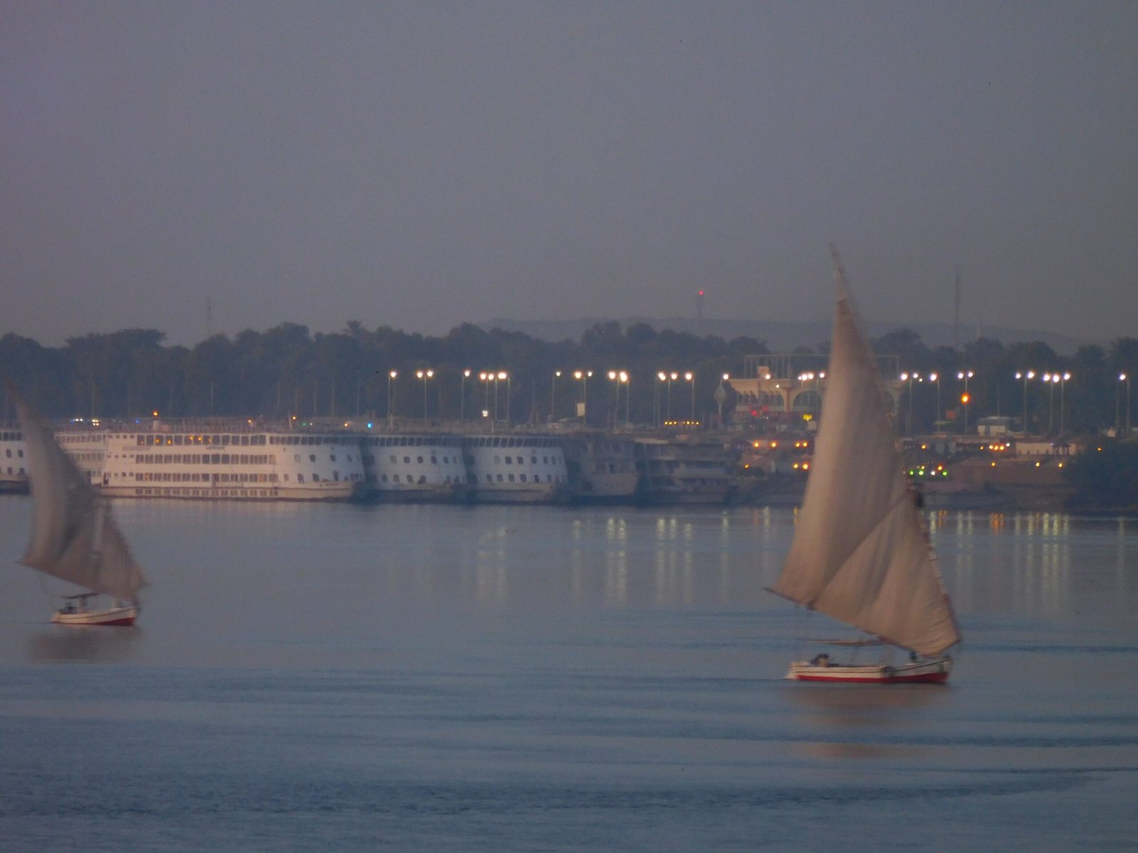 Due feluche sul Nilo all'imbrunire con le navi da crociera illuminate sull'altra riva