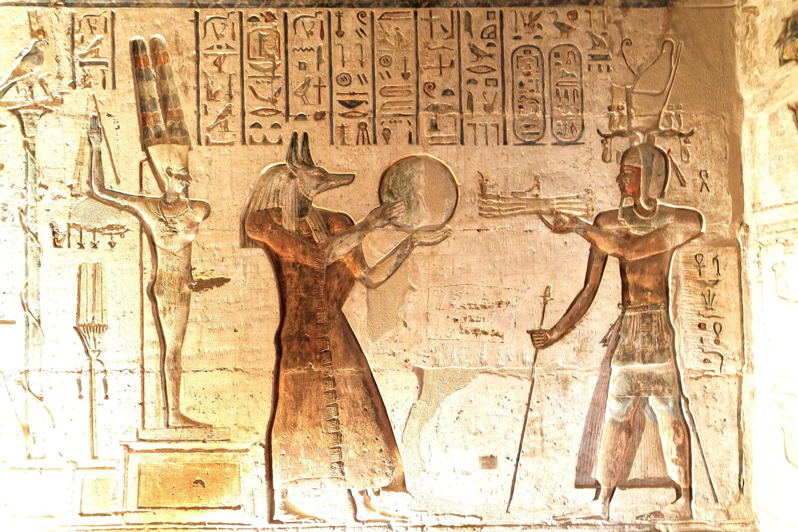 Un rilievo del tempio di Deir el-Medina con Anubi che porge un disco al faraone, tra geroglifici colorati
