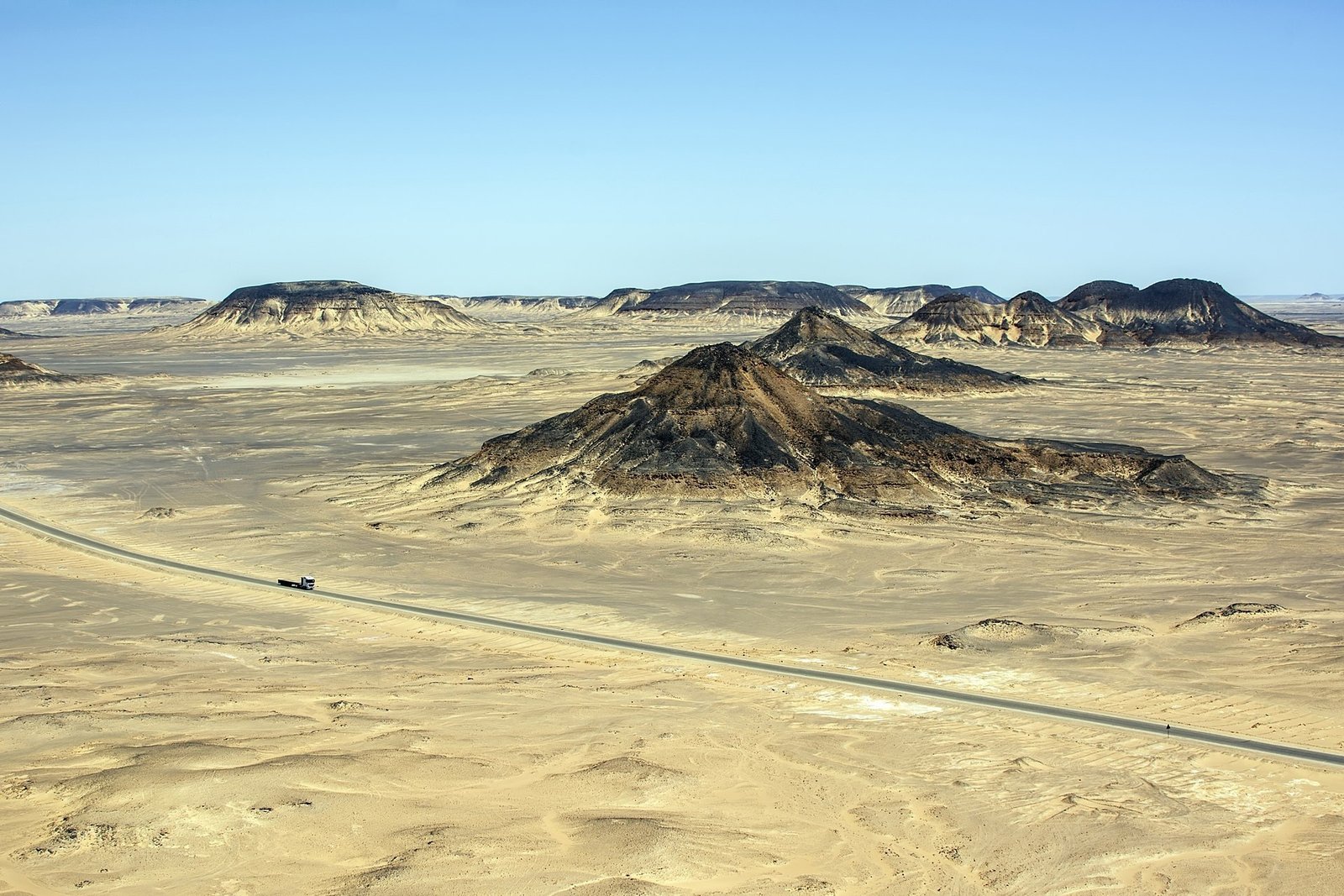 Le colline scure del Deserto Nero vicino a Bahariya, con la strada asfaltata che attraversa la pianura